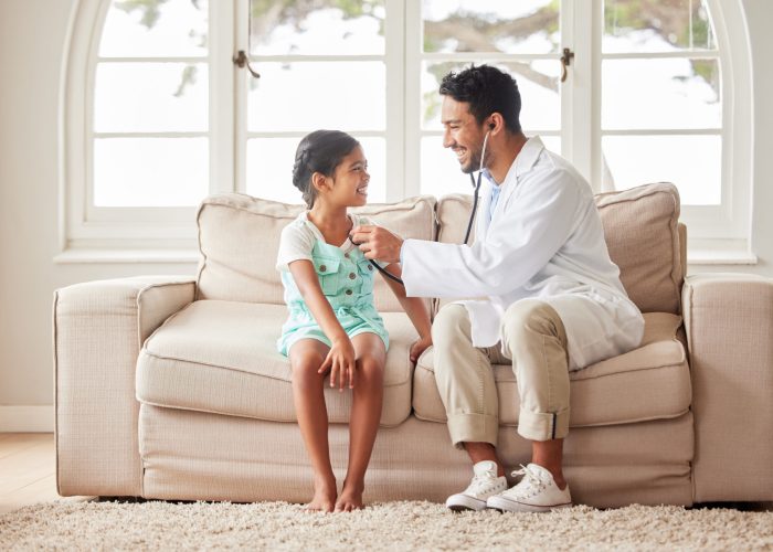 Young handsome smiling doctor using a stethoscope to listen to a sick little girls heartbeat during.